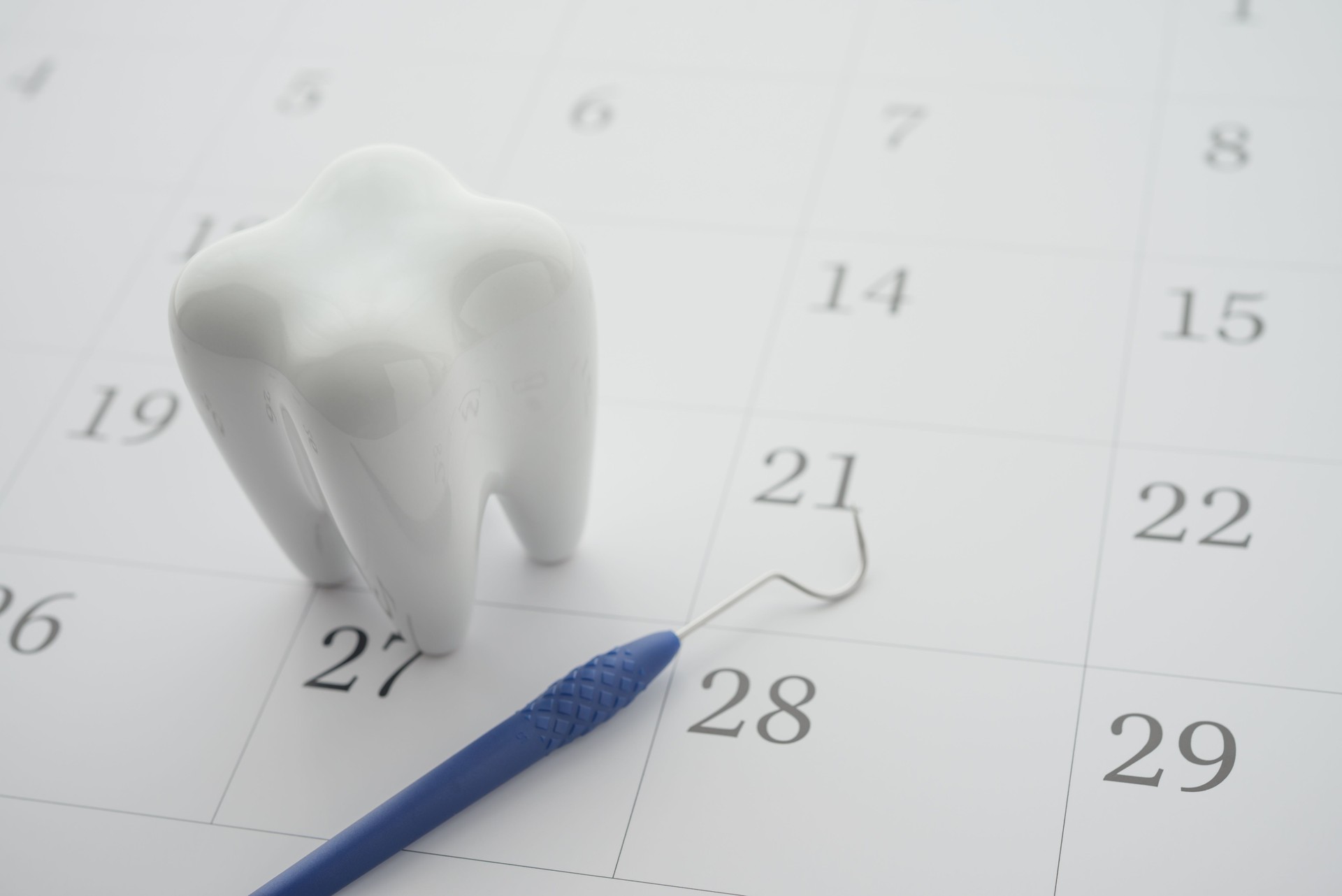 White healthy tooth model and dental pick explorer probe on blank white calendar background with copy space.